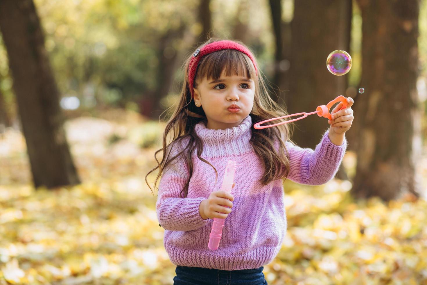 Little girl playing with soap bubbles of autumn leaves in the park photo