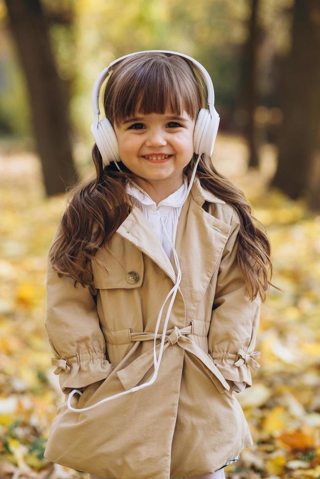 niña feliz escuchando música con auriculares en el parque de otoño. foto