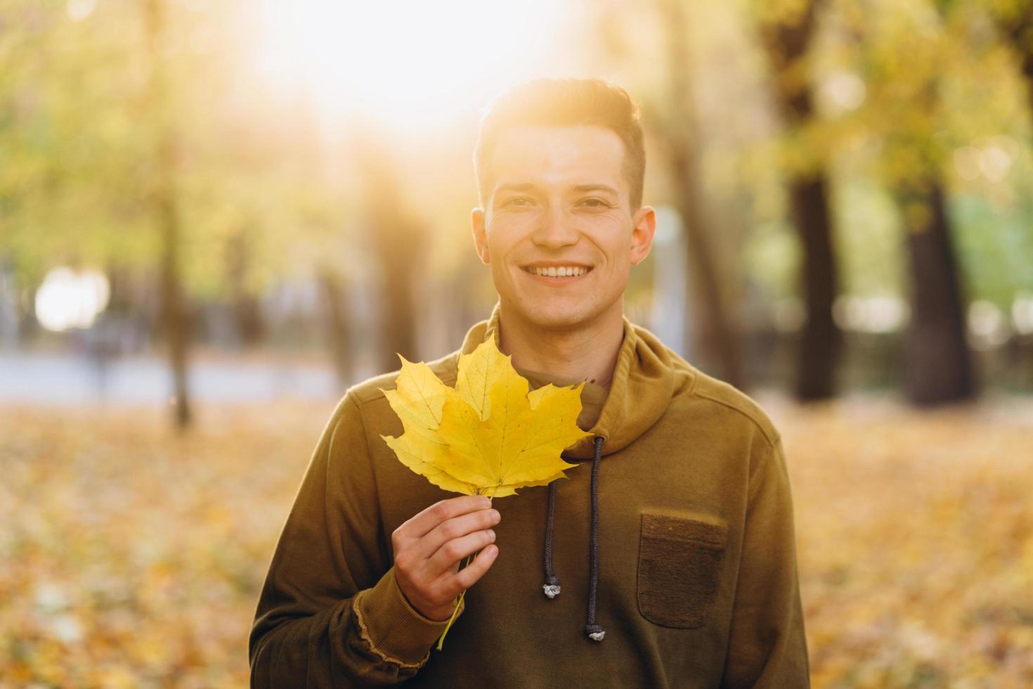 Guy smiling and holding a bouquet of autumn leaves in the park photo