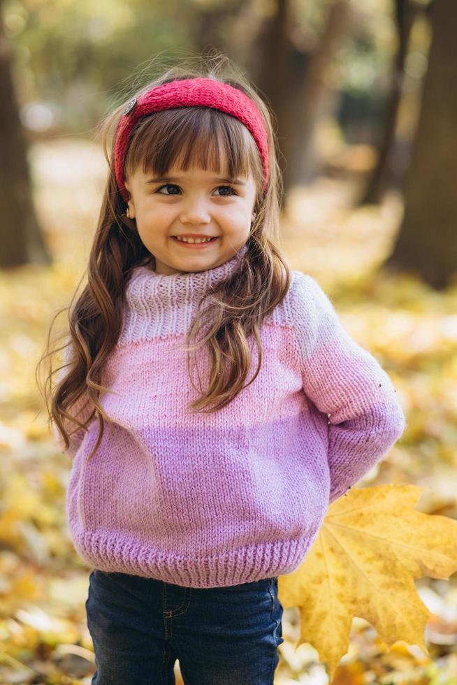 Retrato de una niña feliz sosteniendo una hoja en el parque de otoño foto