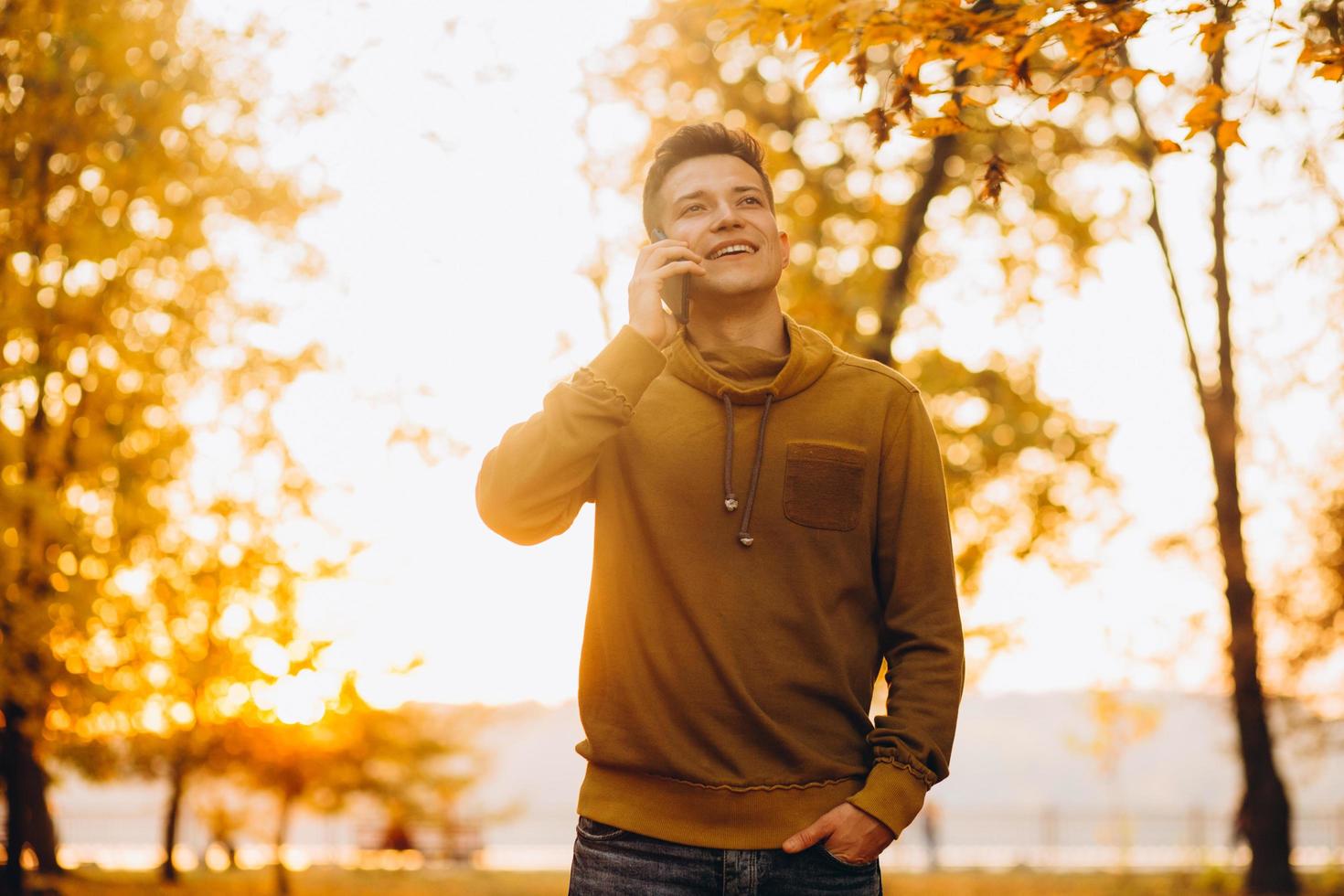 Happy guy smiling and talking on the phone in the autumn park photo