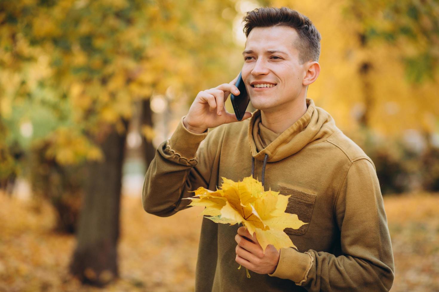 chico feliz sonriendo y hablando por teléfono en el parque de otoño foto