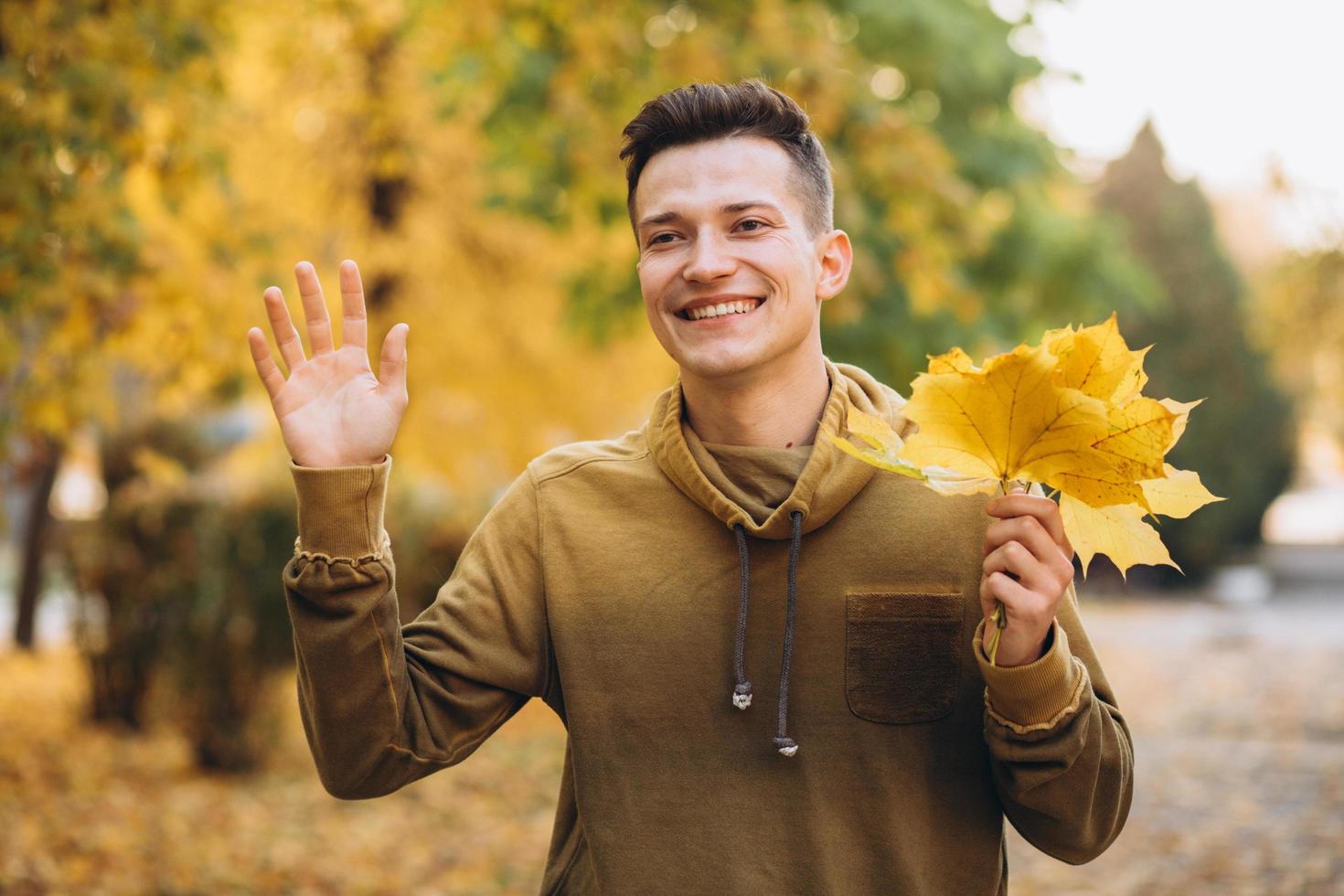 Portrait of handsome and happy guy smiling and greeting in autumn park photo