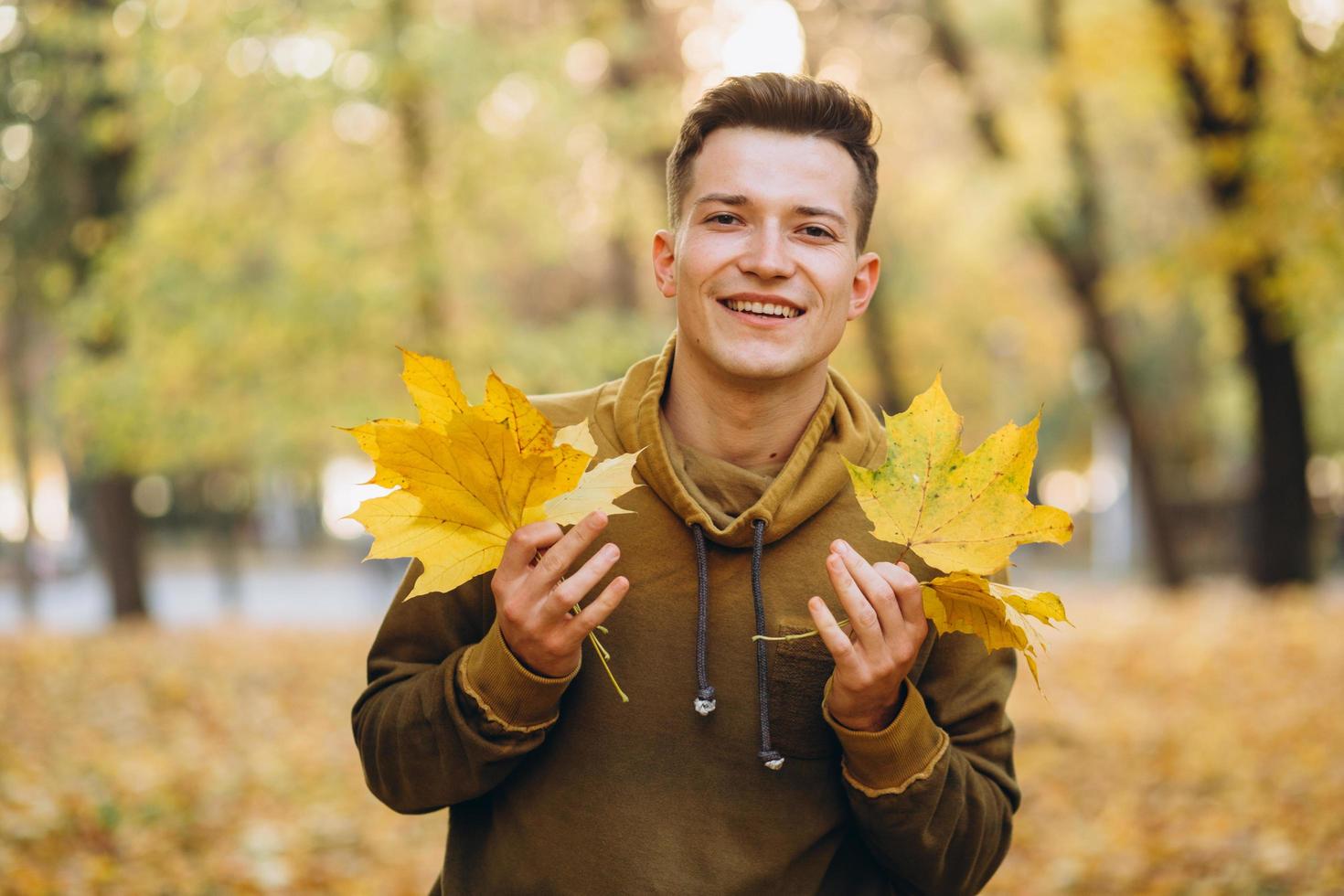 chico sonriendo y sosteniendo un ramo de hojas de otoño en el parque foto