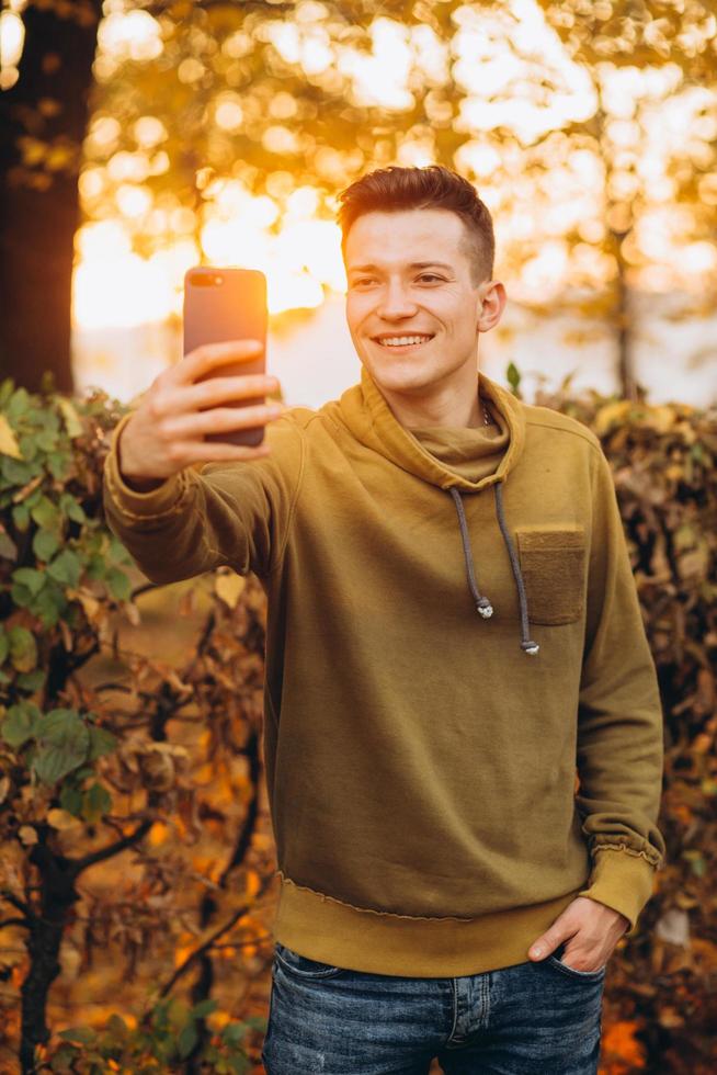 Guy smiling and holding a bouquet of leaves and taking selfie in park photo