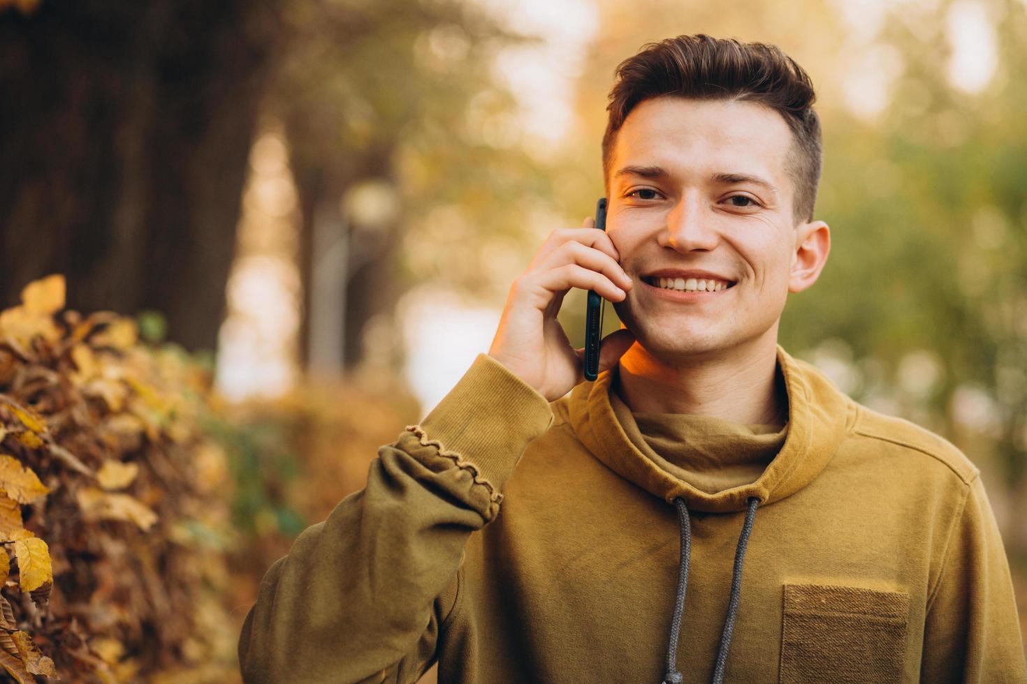 chico feliz sonriendo y hablando por teléfono en el parque de otoño foto