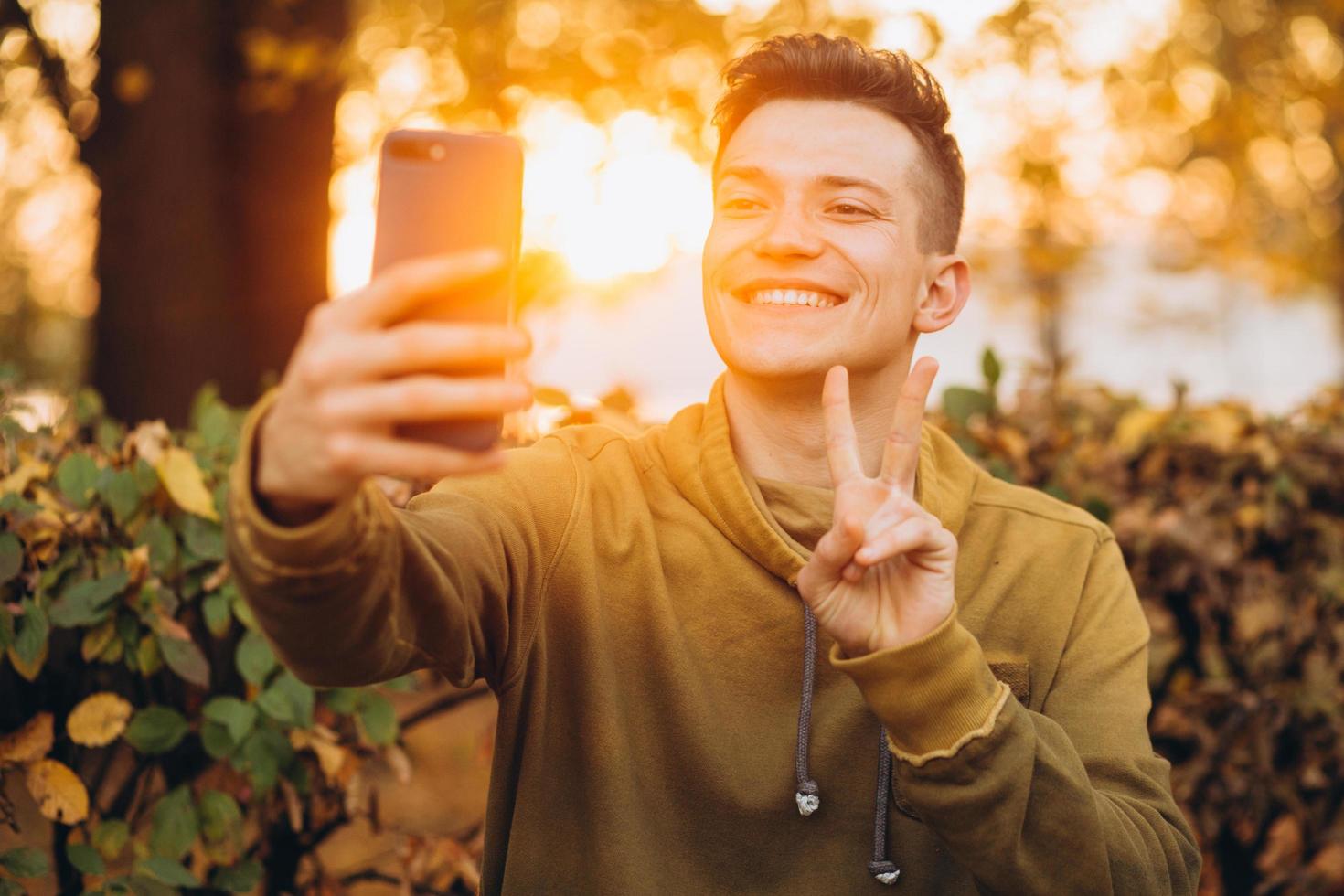 Guy holding a bouquet of autumn leaves and taking a selfie in the park photo