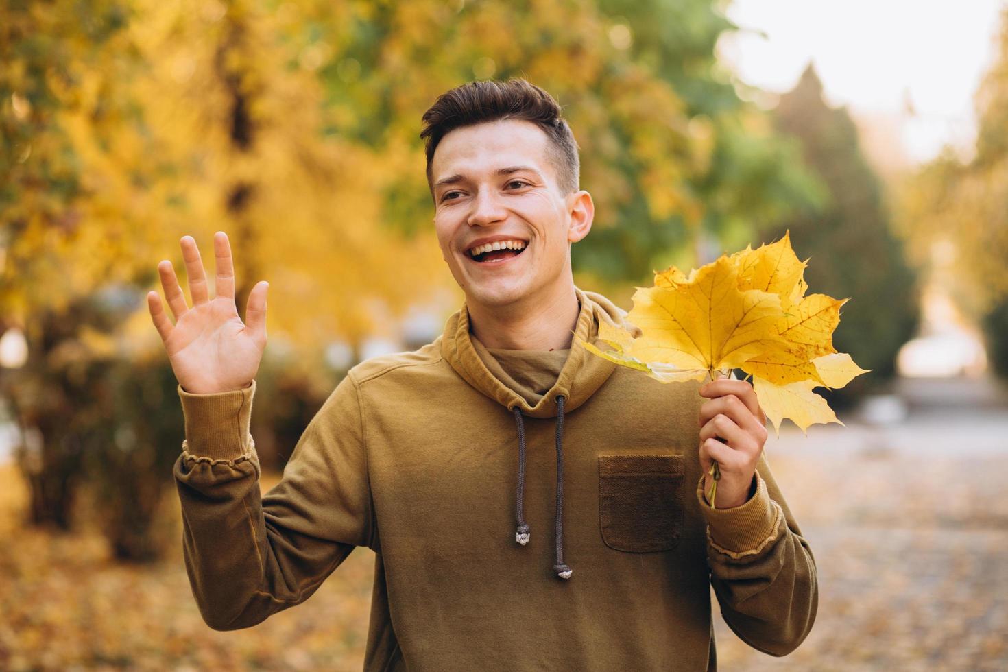 Portrait of handsome and happy guy smiling and greeting in autumn park photo