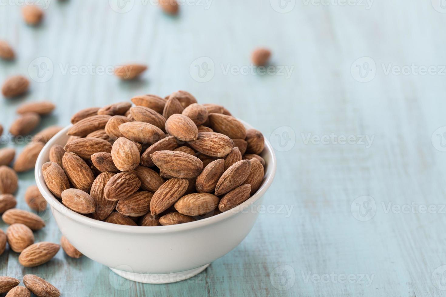 Almonds In White Bowl and Scattered on Blue Wood Background photo