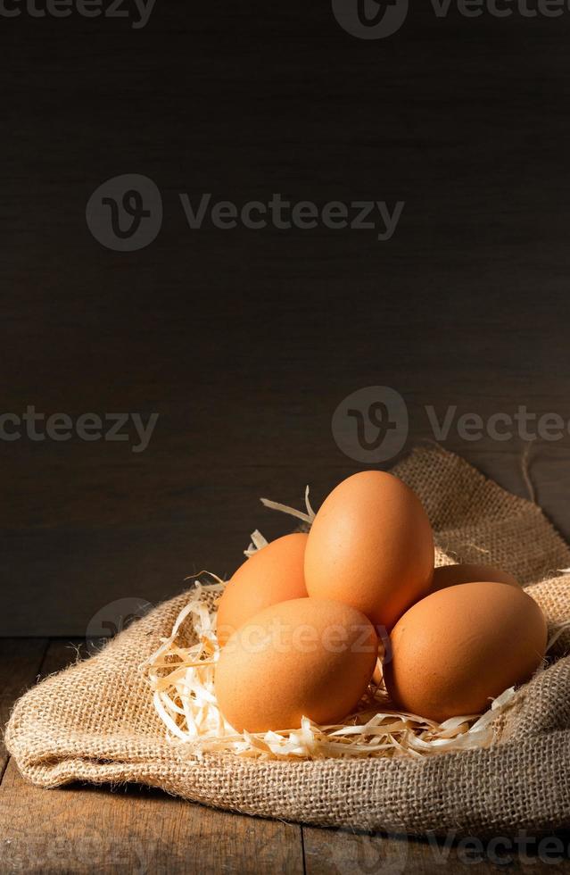 Huevos orgánicos frescos en arpillera con pasto seco sobre mesa de madera foto