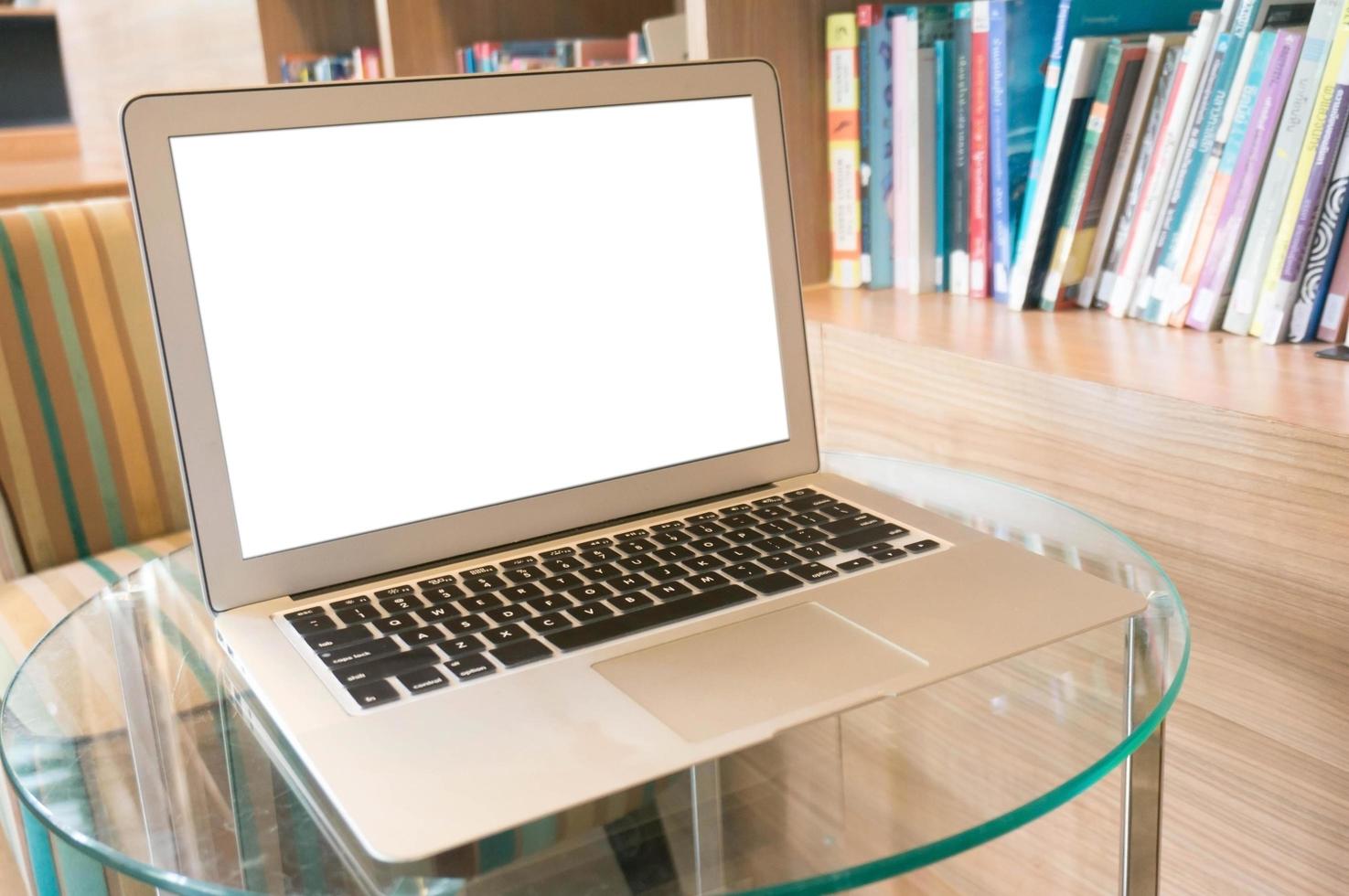 Laptop with blank screen on wooden table in front of library photo