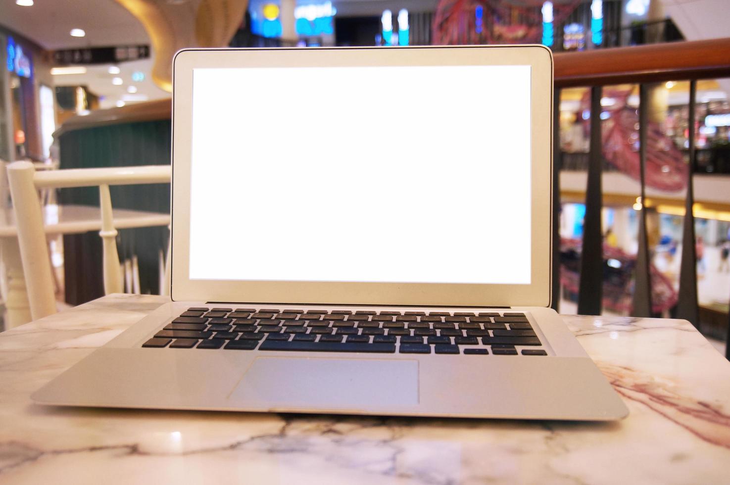 Laptop with blank screen on wooden table in front of coffeeshop cafe photo