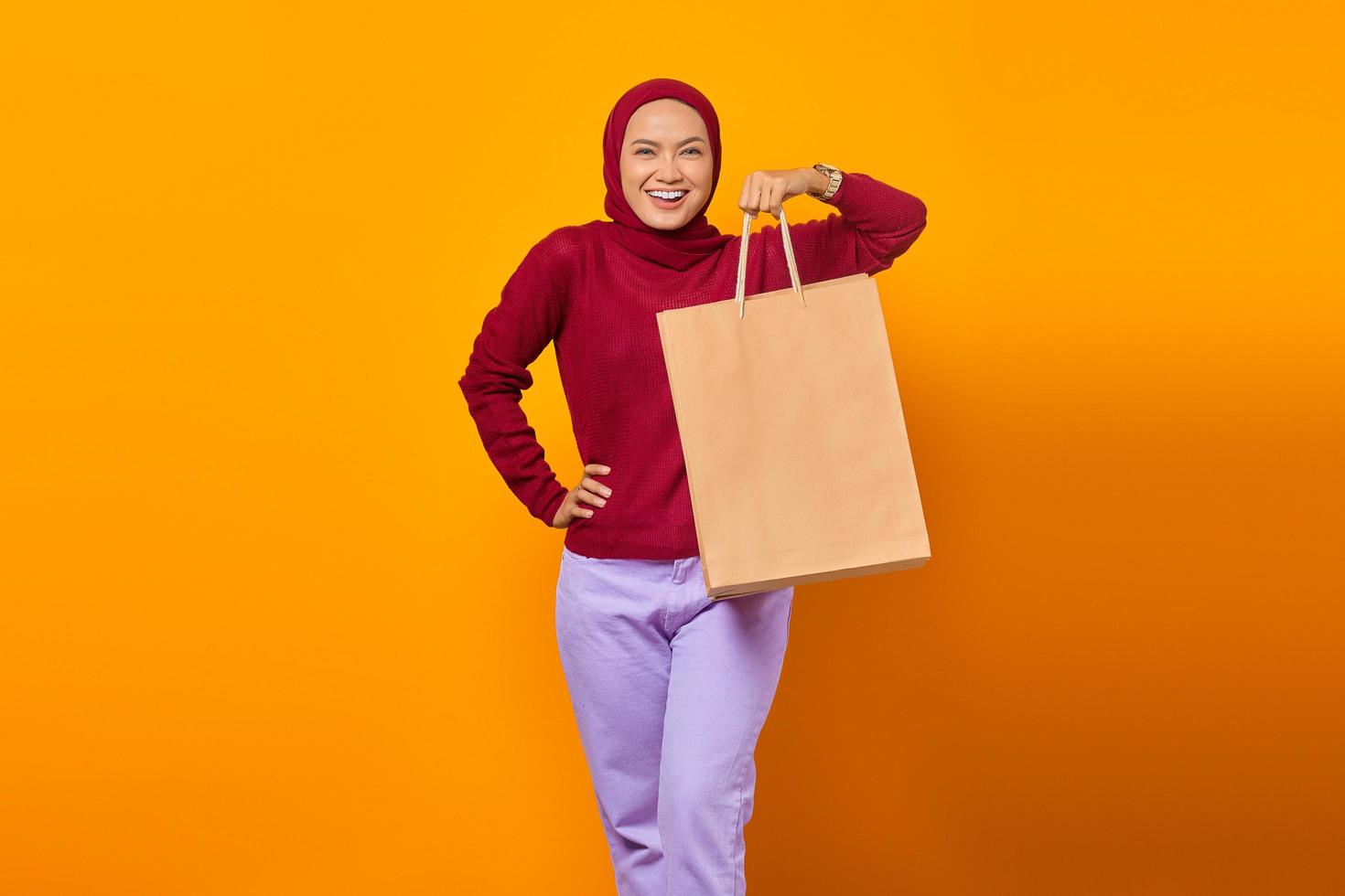 Alegre mujer asiática sosteniendo bolsas de la compra sobre fondo amarillo foto