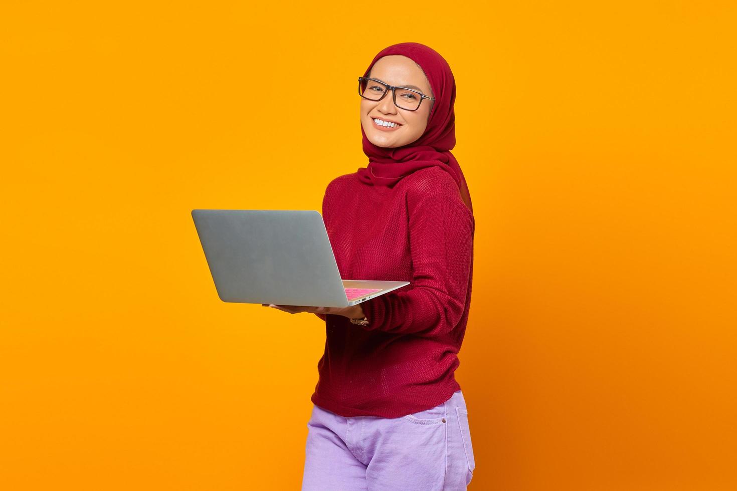 Retrato de mujer asiática sonriente sosteniendo portátil sobre fondo amarillo foto