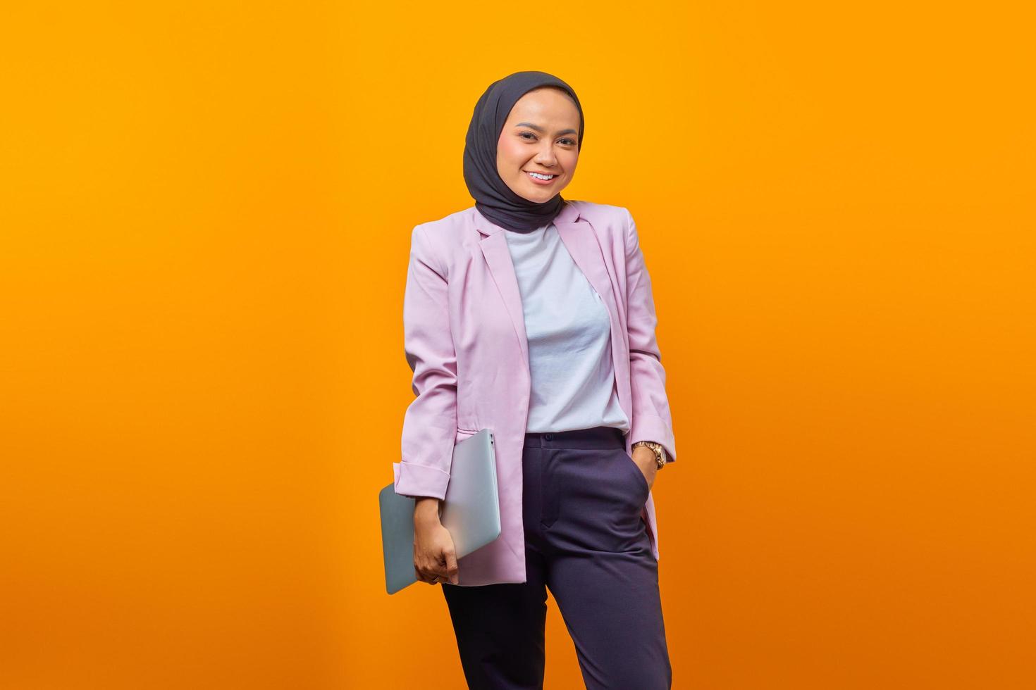 Portrait of smiling Asian woman holding laptop on yellow background photo