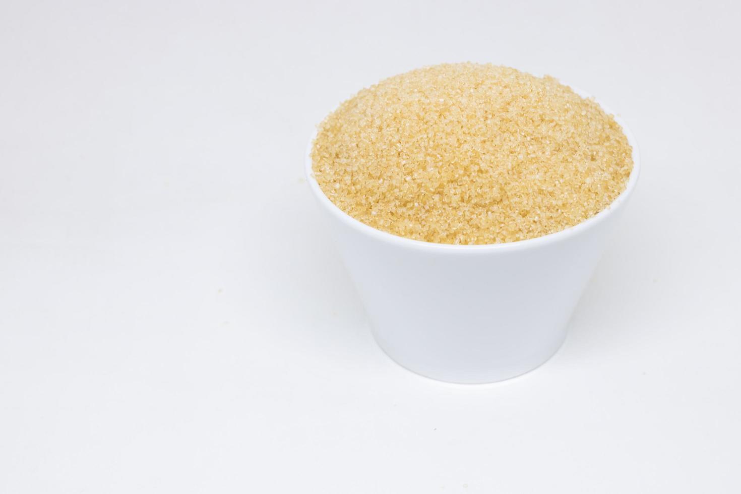Azúcar morena en una taza blanca sobre un fondo blanco. foto