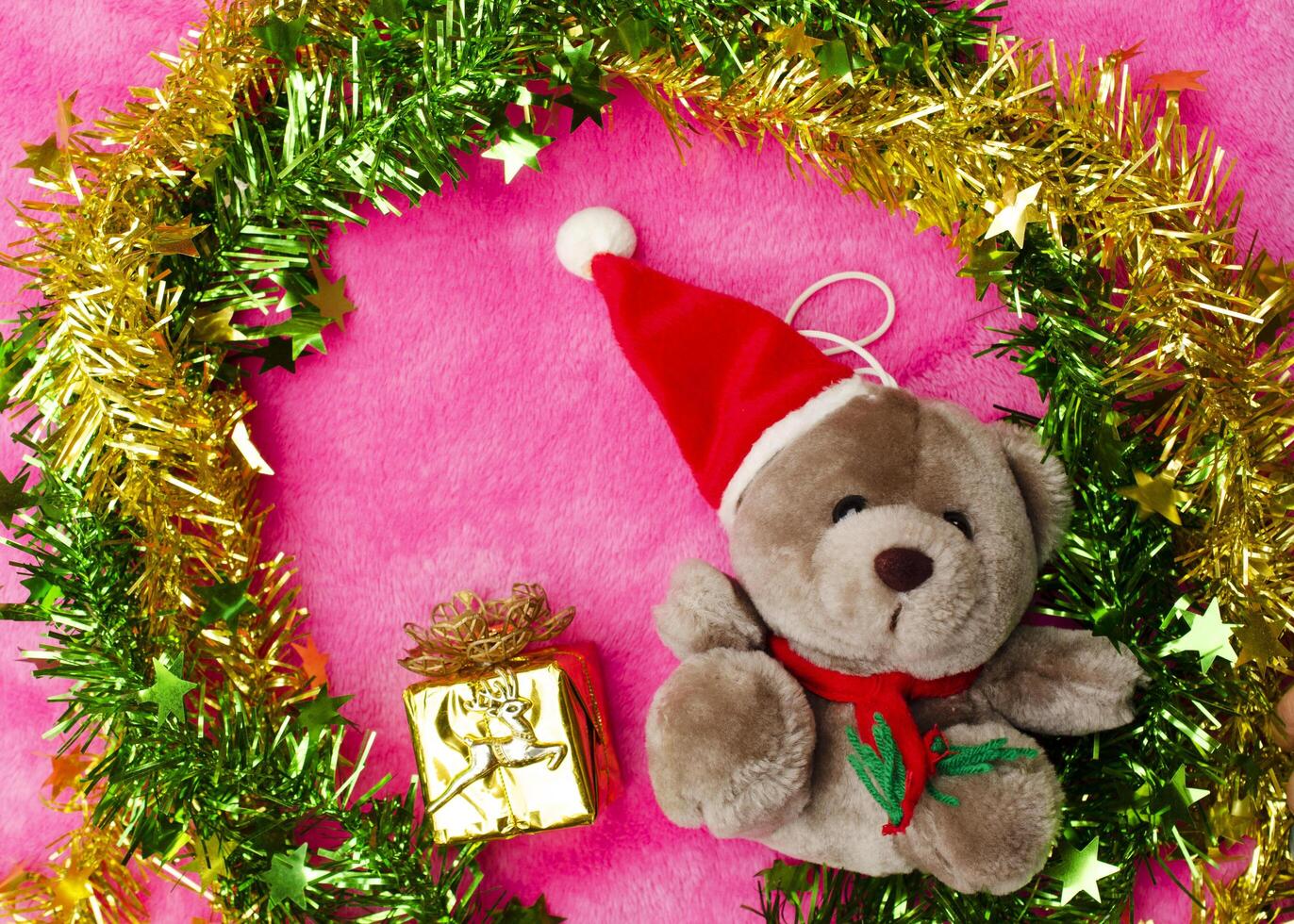 Peluche con gorro de navidad y decoración sobre fondos de color rosa arriba foto