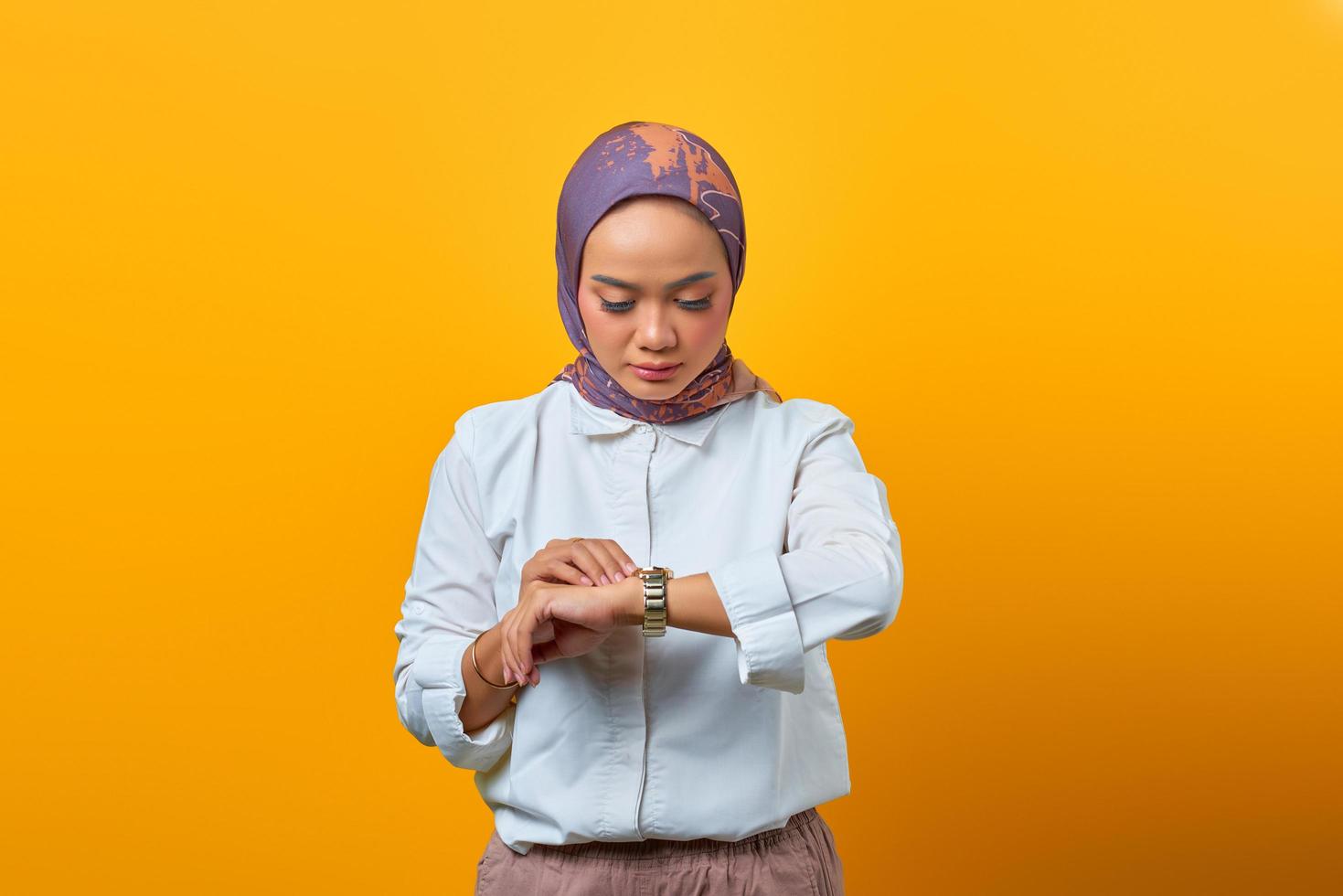 Beautiful Asian woman checking time on watch over yellow background photo