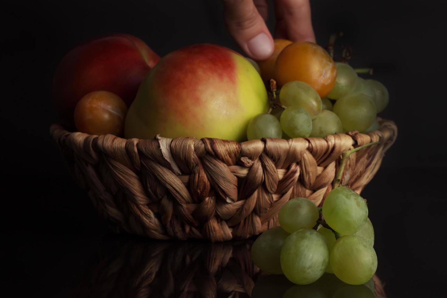 frutos de uvas, ciruelas y una manzana en una canasta de mimbre foto