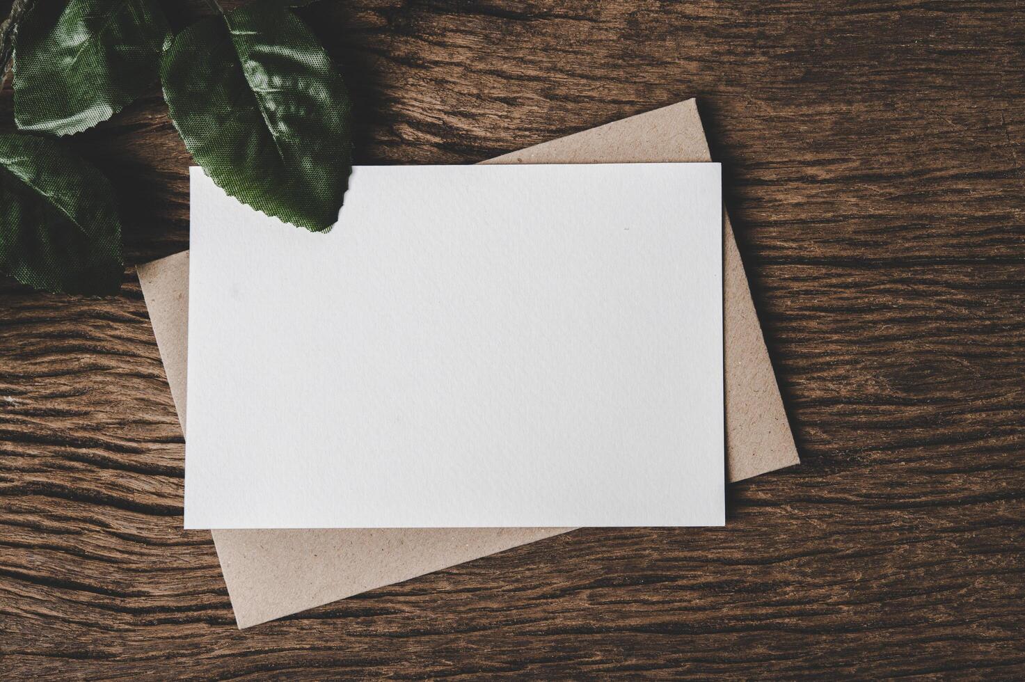 A blank card is placed on envelope and leaf with wood background photo