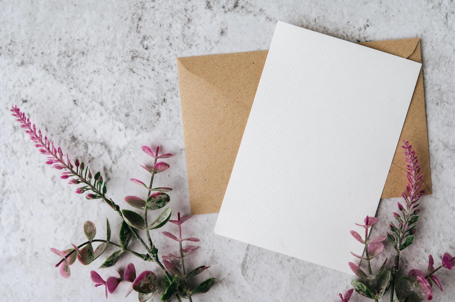 Se coloca una tarjeta en blanco con sobre y flor sobre fondo blanco. foto