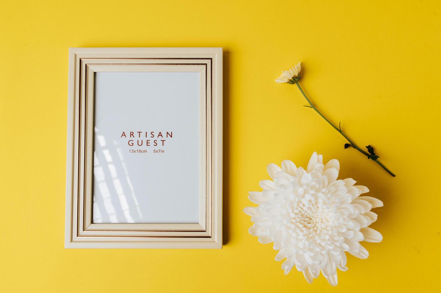 White photo frame and flower is placed on yellow background