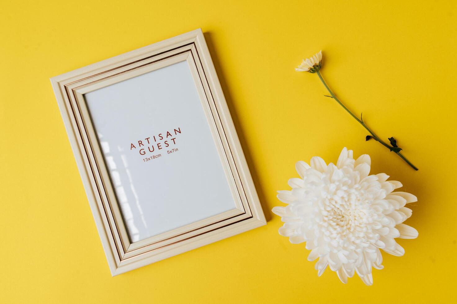 White photo frame and flower is placed on yellow background