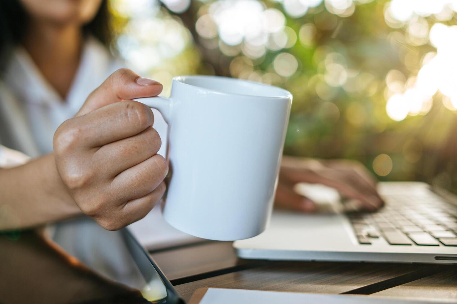 white cup on hand, and laptop on the table photo