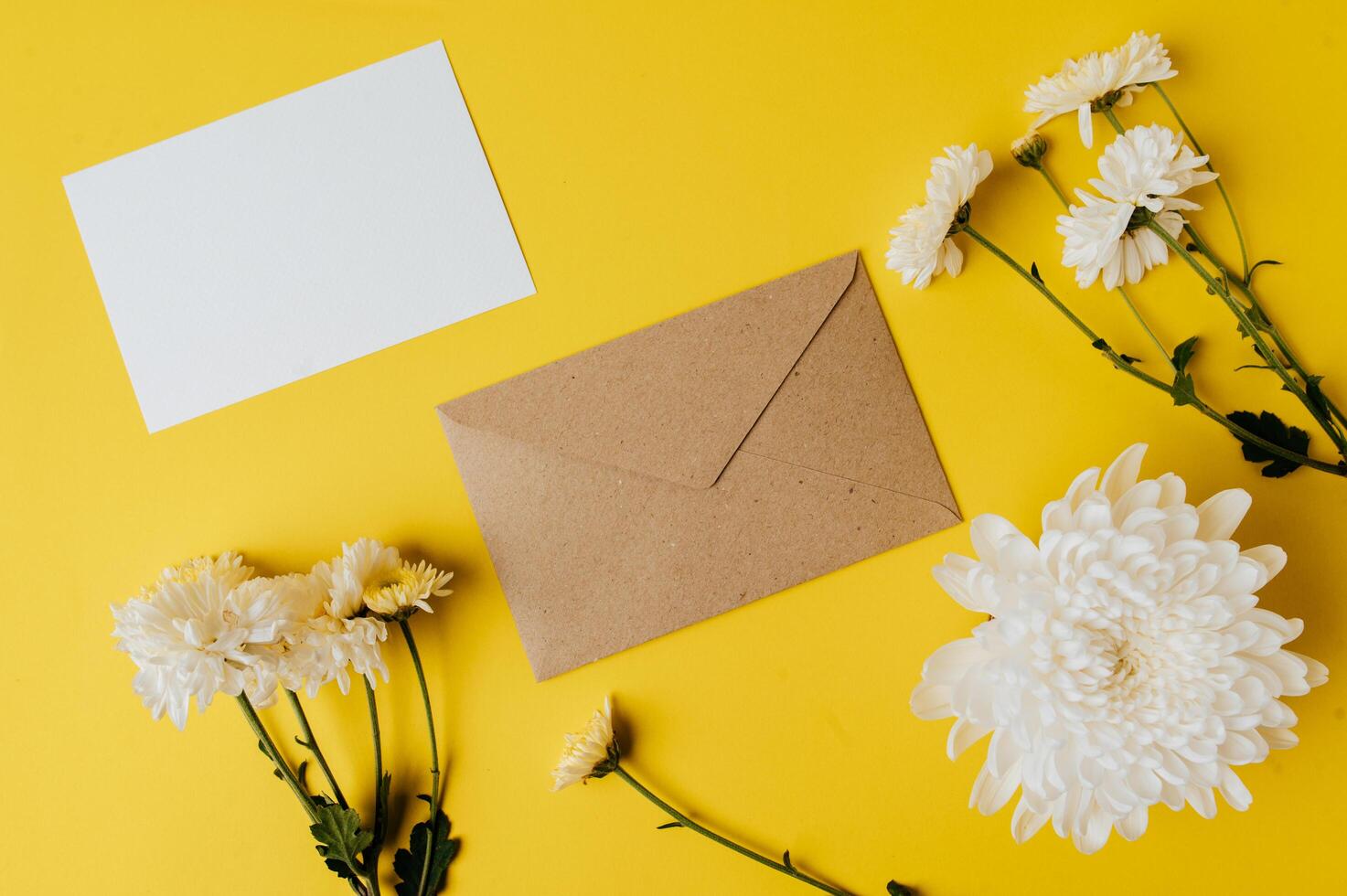 Se coloca una tarjeta en blanco con sobre y flores sobre fondo amarillo. foto