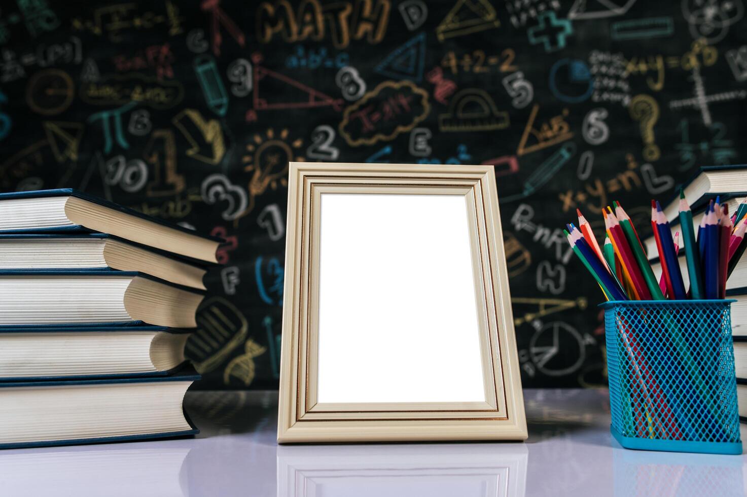 white photo frame, book and colored pencils in classroom