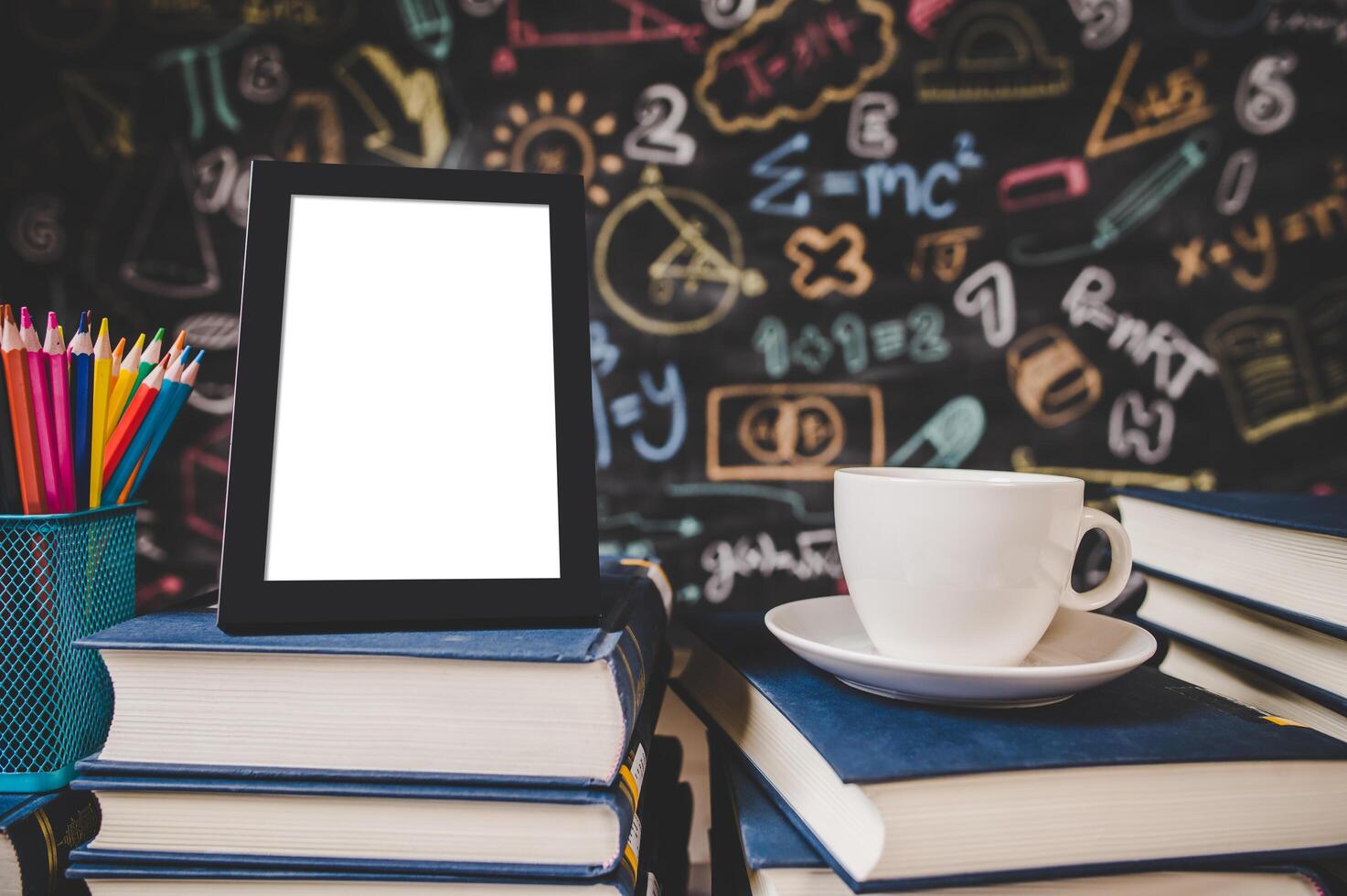 Marco de fotos negro y taza en libros en el aula con lápices de colores.