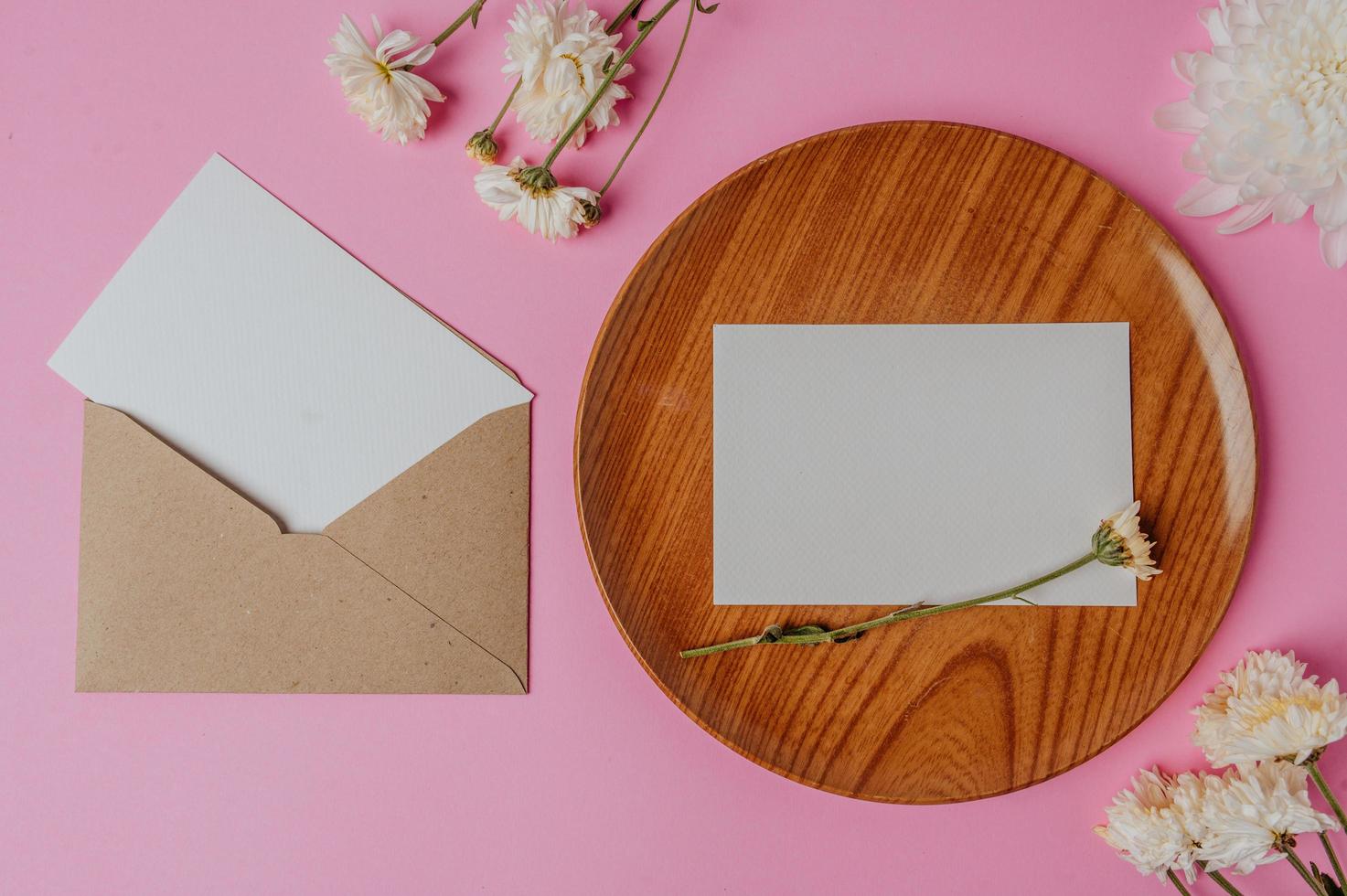 Sobre marrón, flor y tarjeta en blanco sobre placa de madera foto