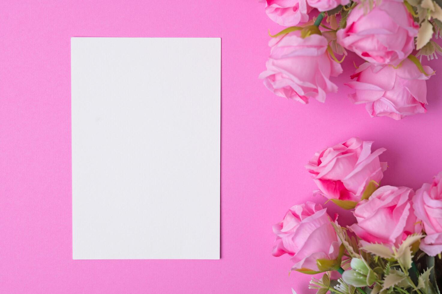 Blank paper with flowers placed on a pink background photo