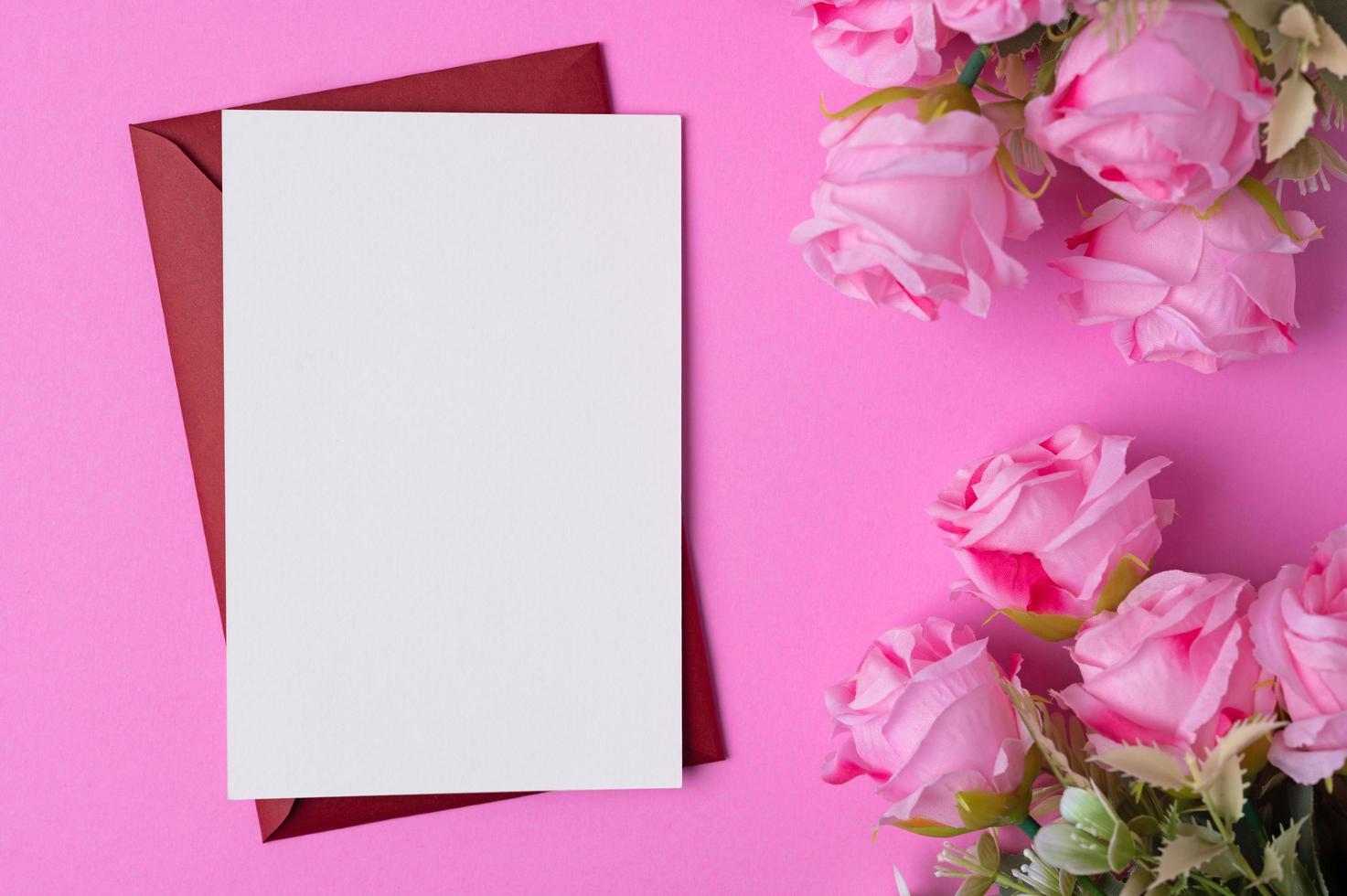 papel en blanco con flores colocadas sobre un fondo rosa foto