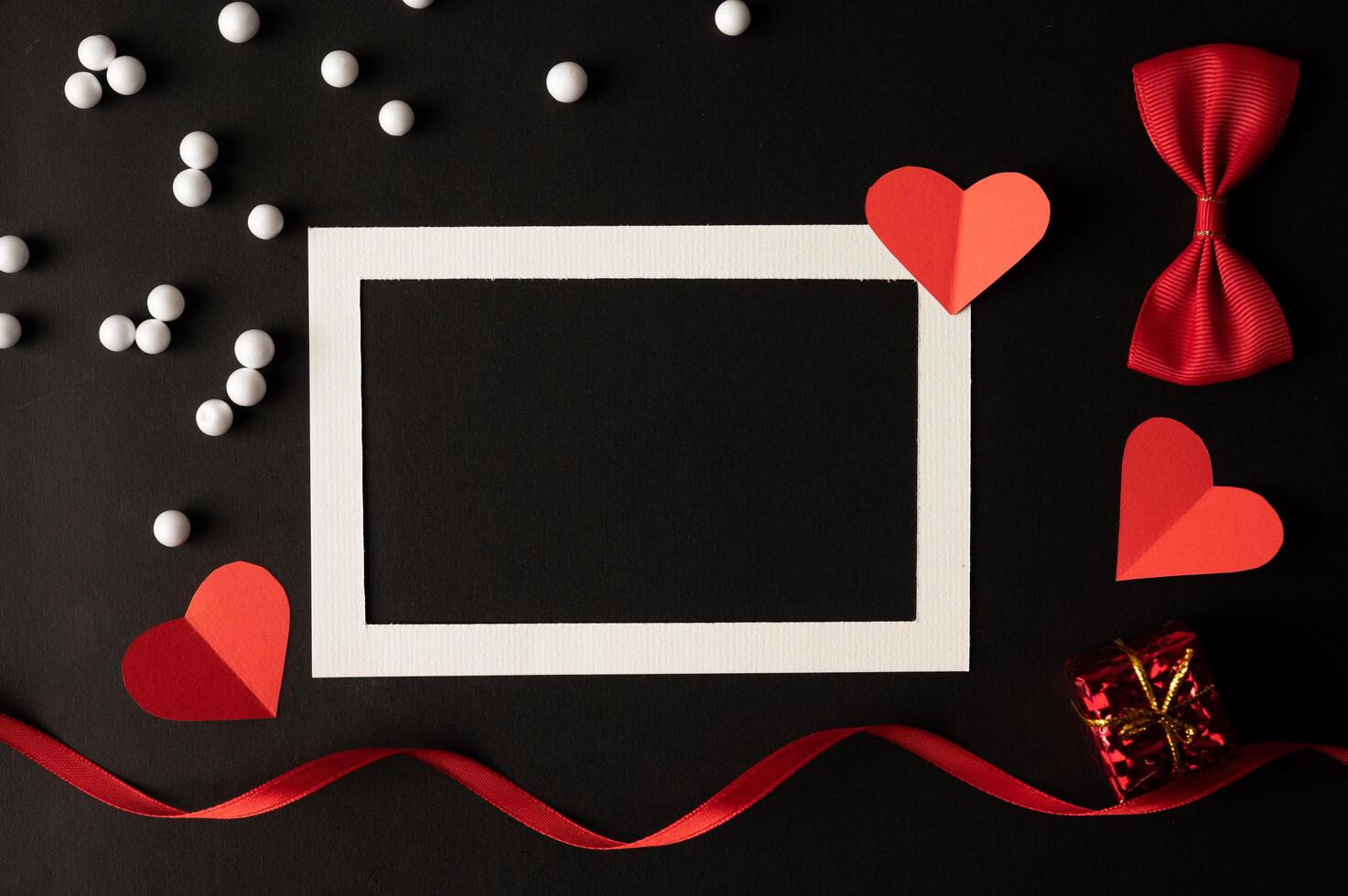 White photo frame and red heart paper pasted on a black background.