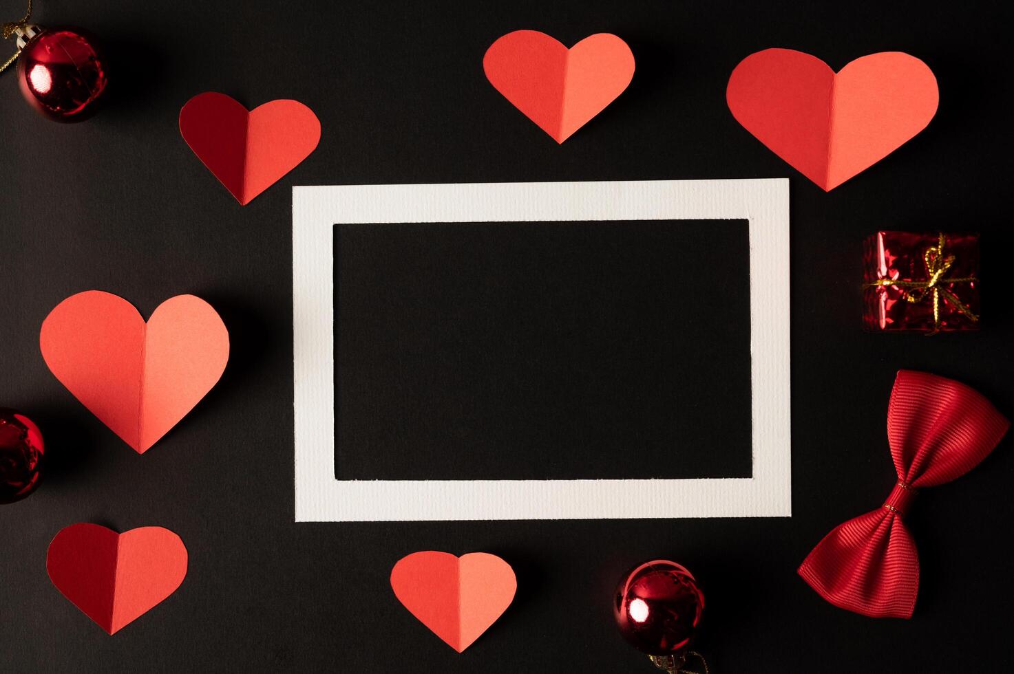 White photo frame and red heart paper pasted on a black background.