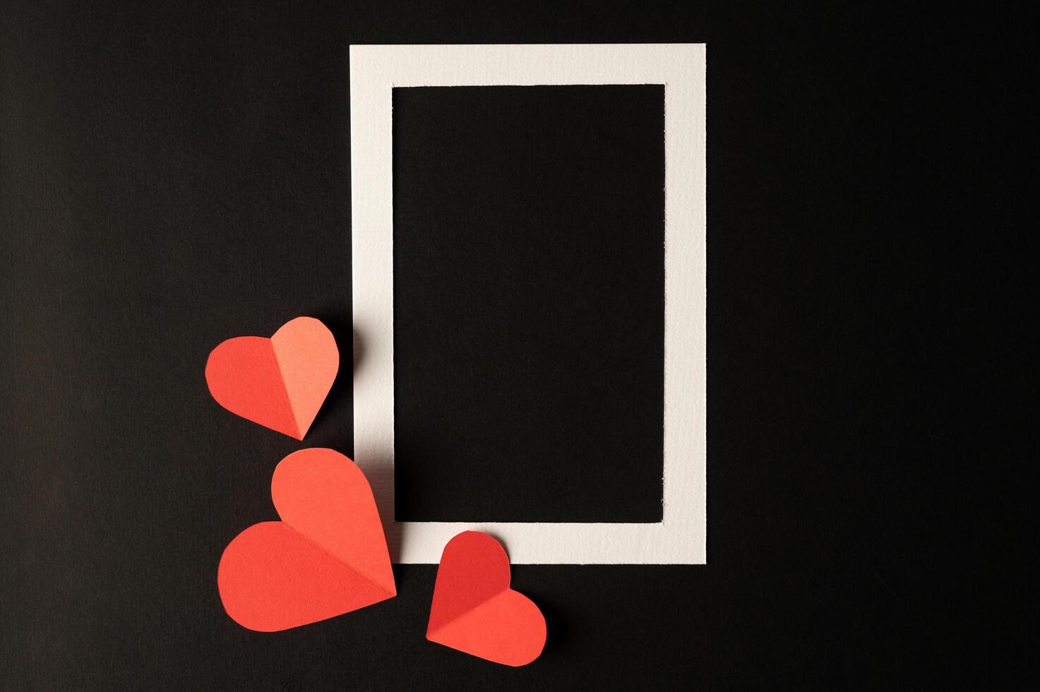 White photo frame and red heart paper pasted on a black background.