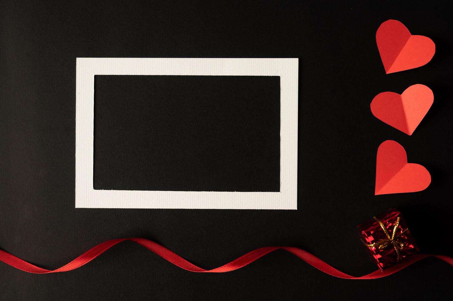 White photo frame and red heart paper pasted on a black background.