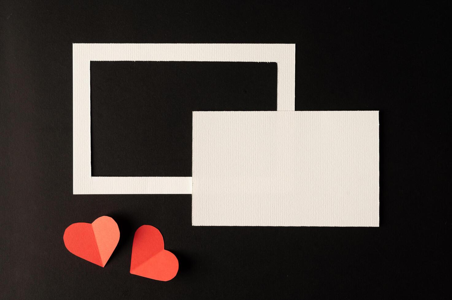 White photo frame and red heart paper pasted on a black background.