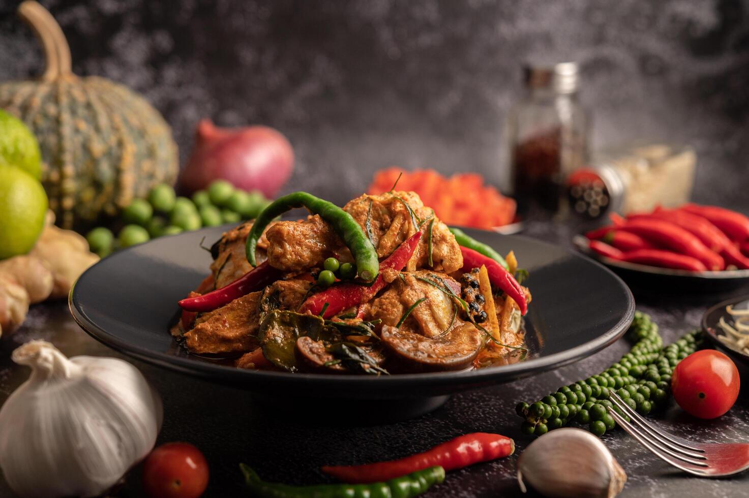 Stir-fried spicy Catfish in black plate with spices on black cement. photo