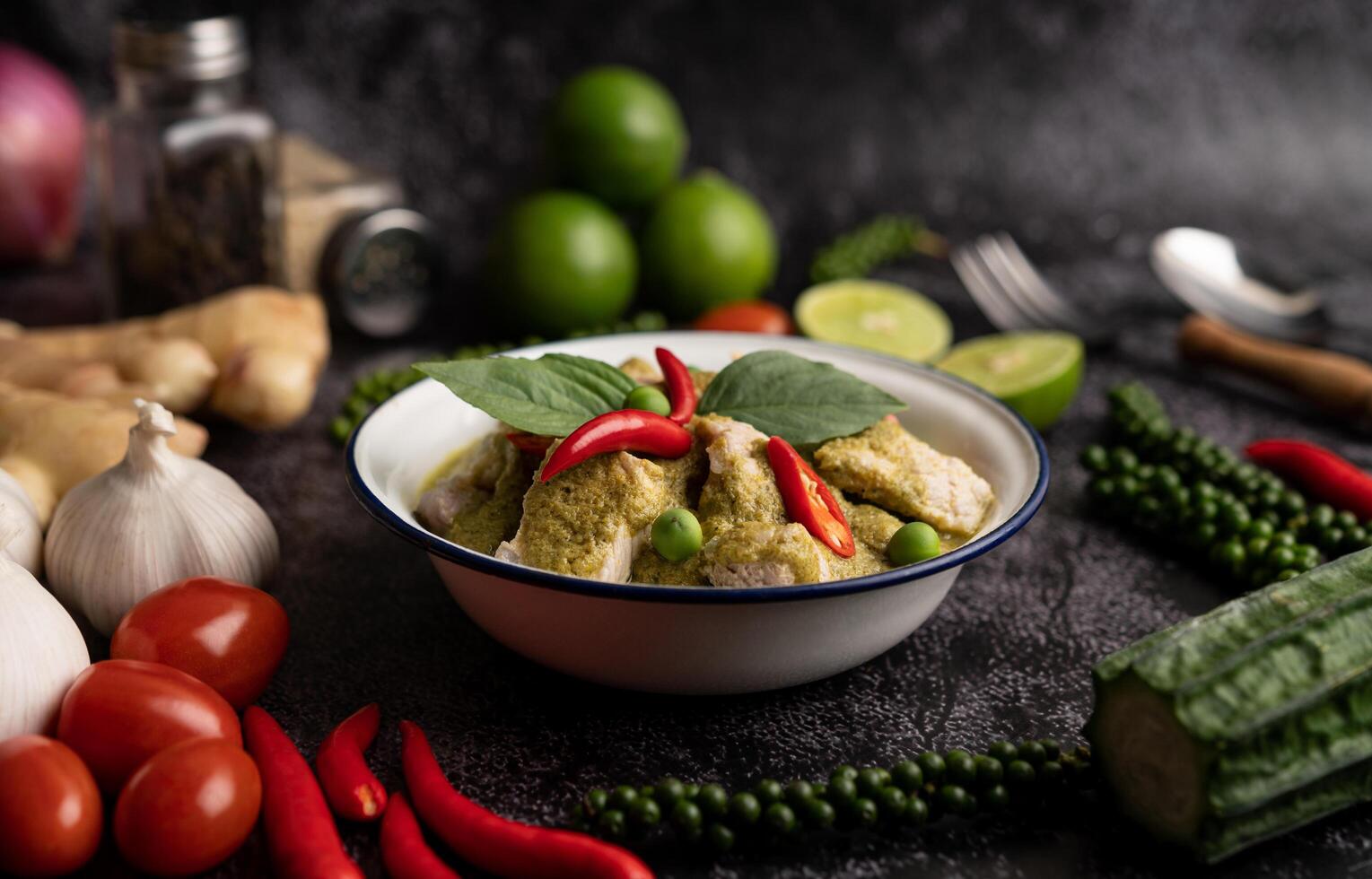 Pork green curry in a white bowl with spices on a black cement photo