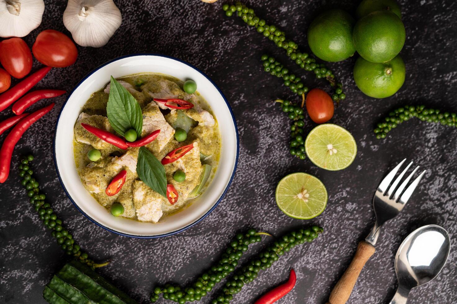 Pork green curry in a white bowl with spices on a black cement photo