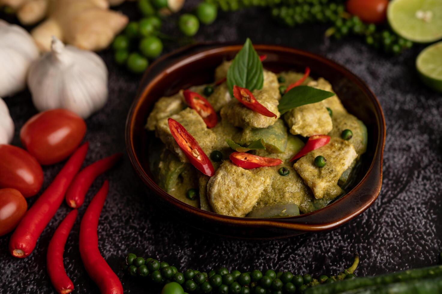 Curry de cerdo verde en un recipiente marrón con especias sobre un cemento negro foto