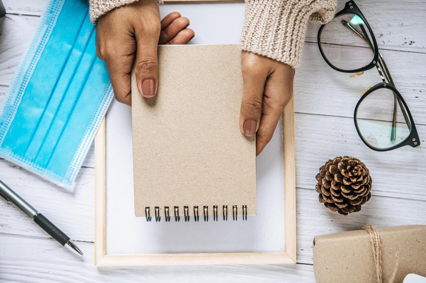 una mano sosteniendo un cuaderno con gafas, bolígrafos y un pequeño regalo foto