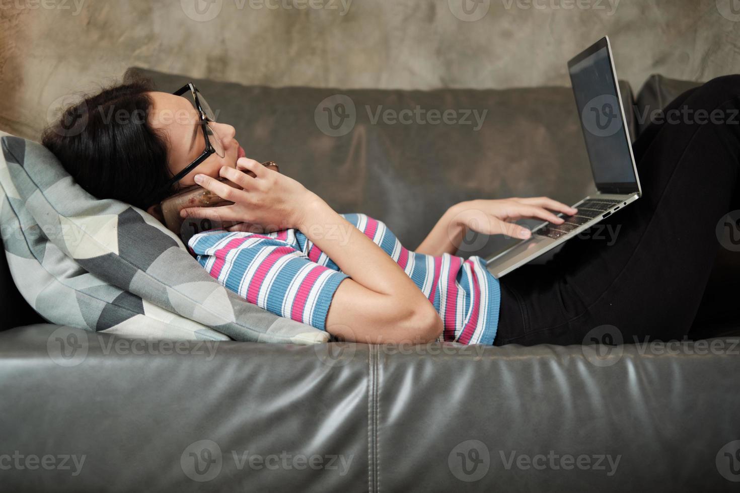 Asian woman working at home, lying down, and using a mobile phone. photo