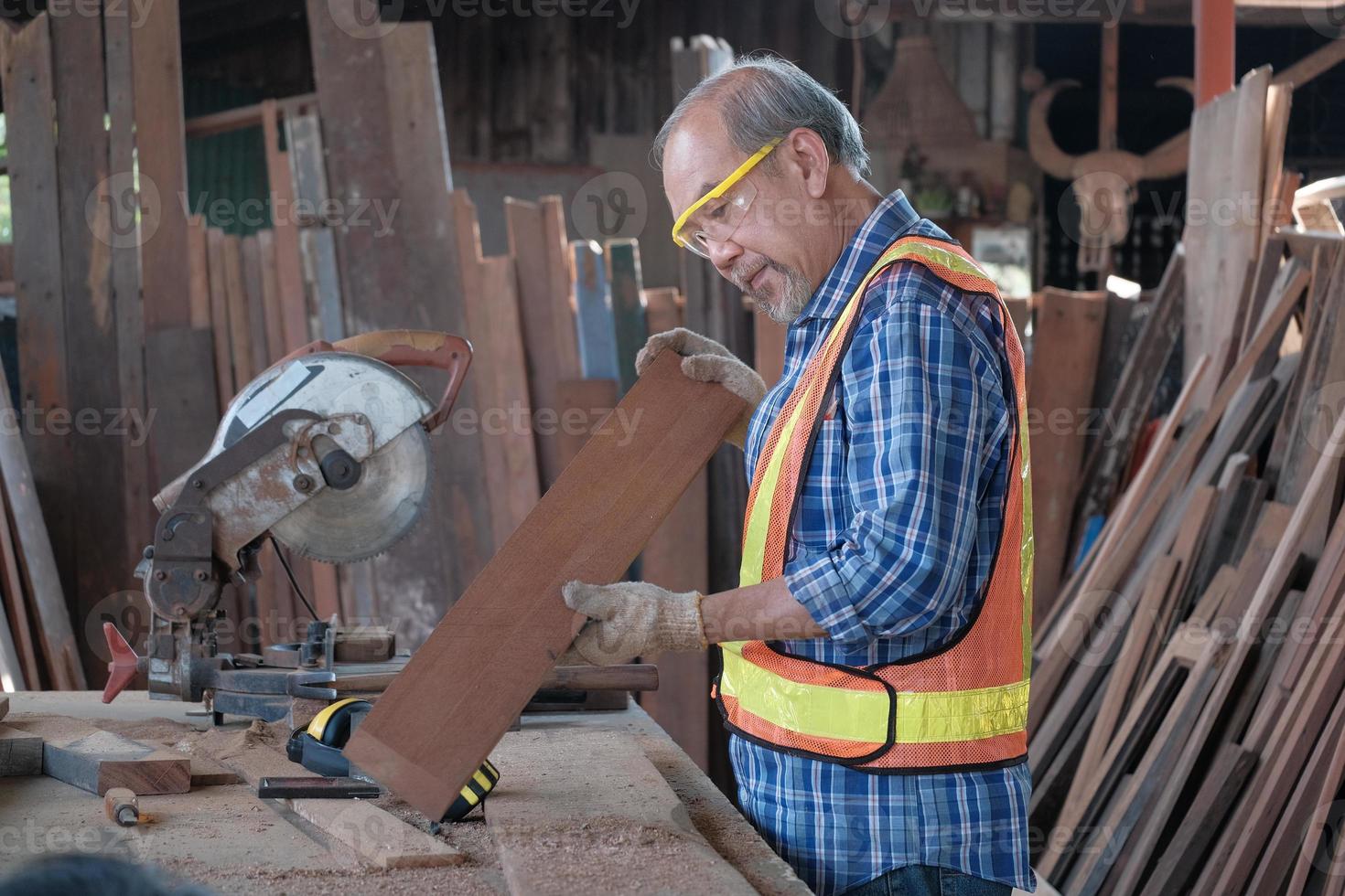 Carpintero asiático senior cortando madera en la fábrica. foto