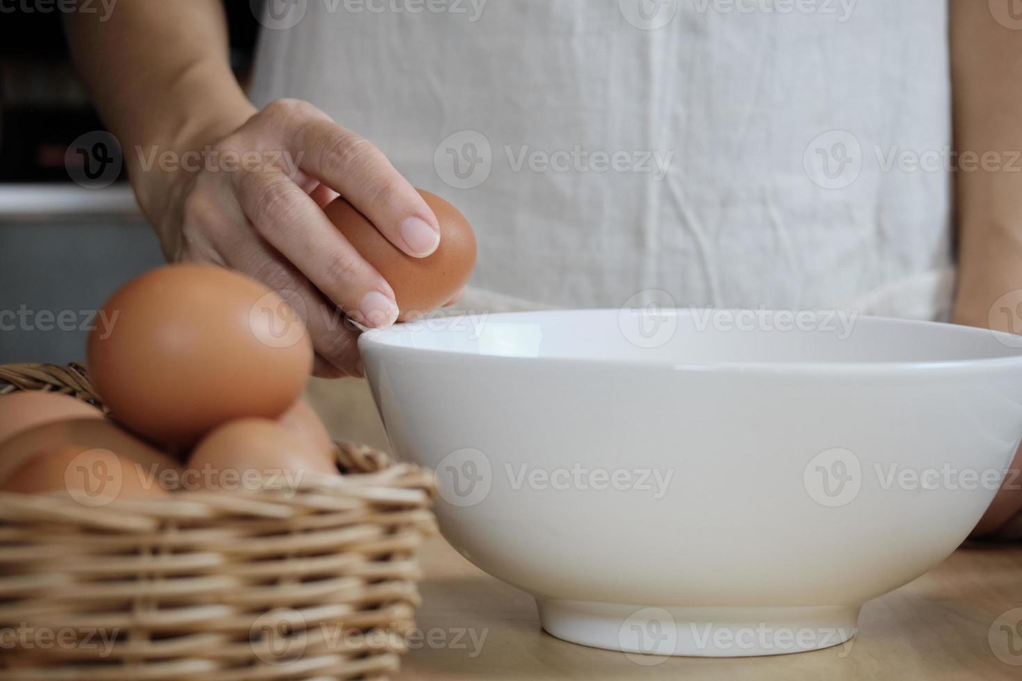 Female cook in a white apron is cracking an egg in home's kitchen. photo