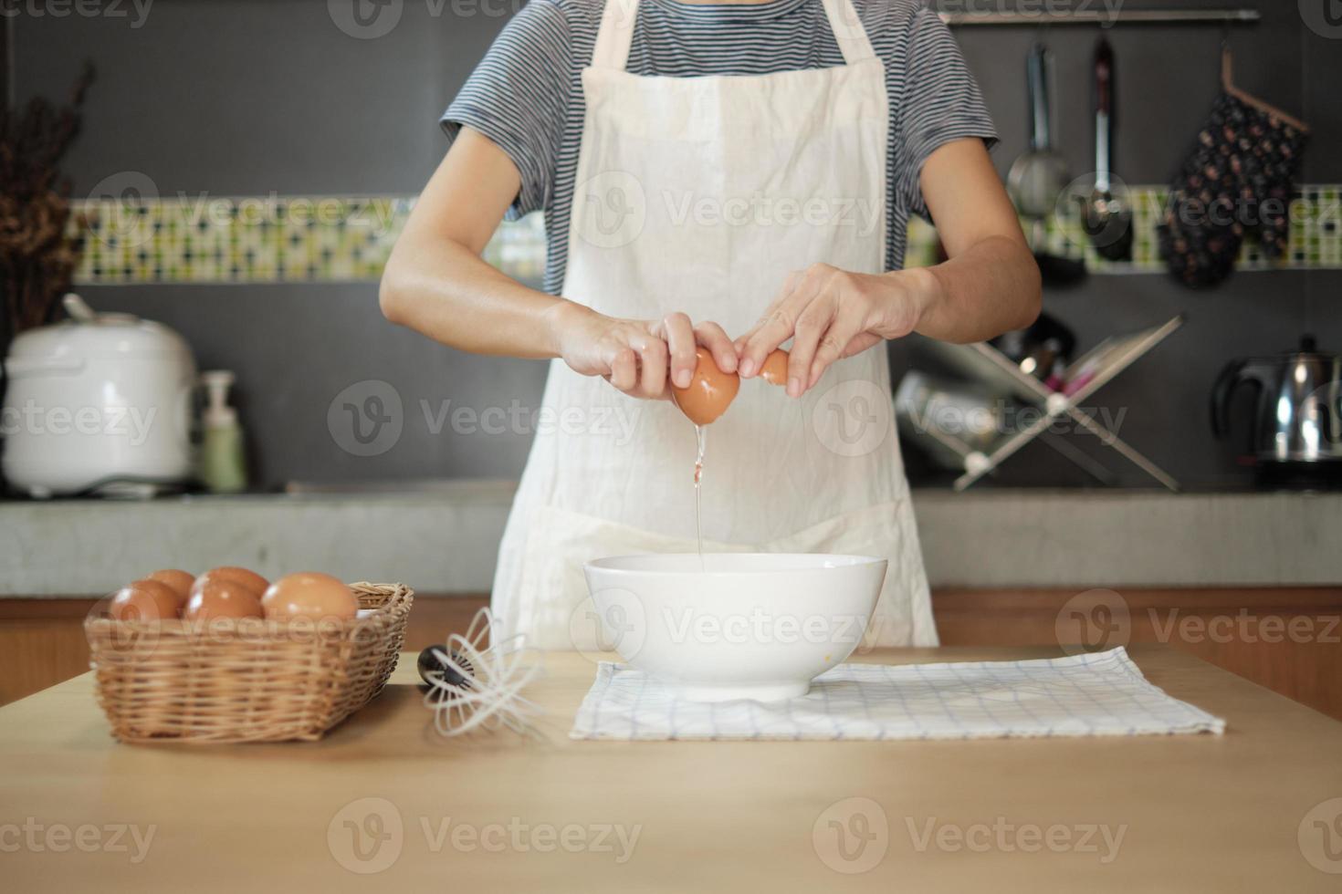 Female cook in a white apron is cracking an egg in home's kitchen. photo