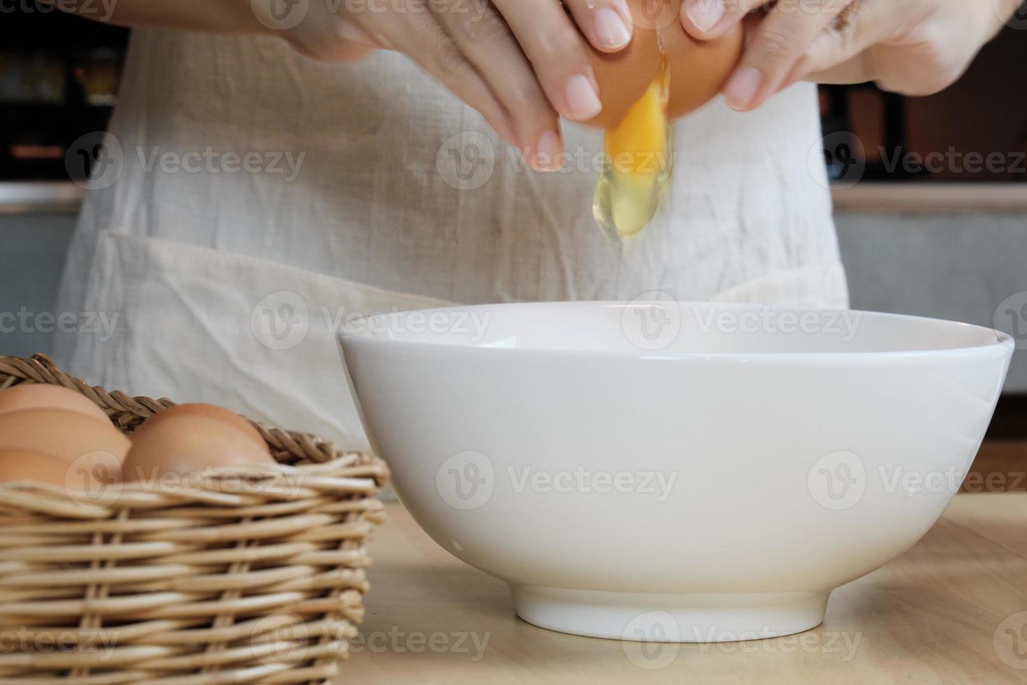 Female cook in a white apron is cracking an egg in home's kitchen. photo