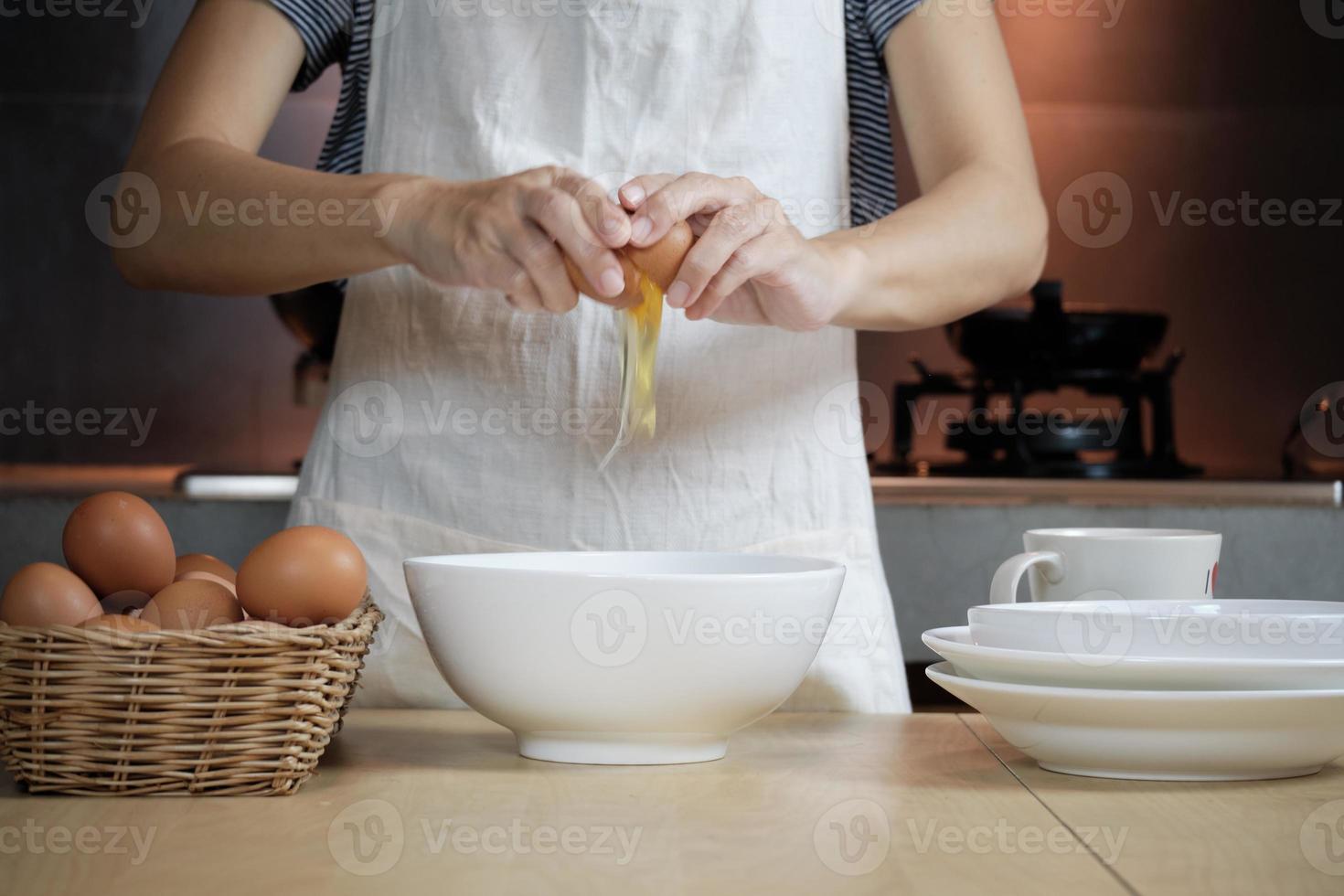cocinera con un delantal blanco está rompiendo un huevo en la cocina de casa. foto